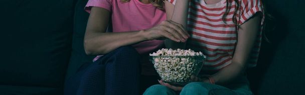 cropped view of mother and daughter watching tv and eating popcorn, panoramic shot - Фото, изображение