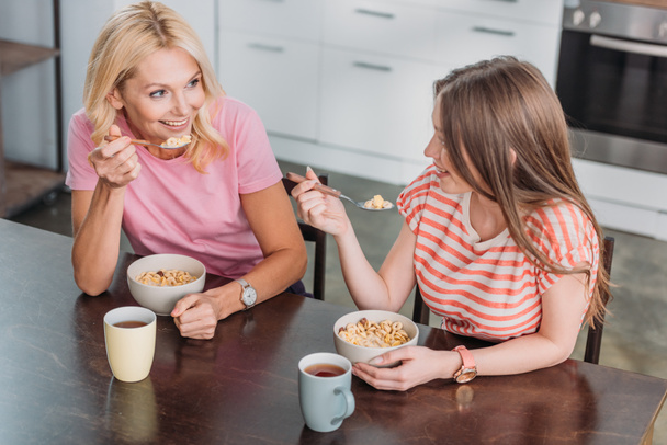 весела мати і дочка розмовляють, сидячи за кухонним столом і снідаючи
 - Фото, зображення