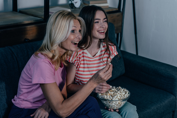 exticed moeder en dochter kijken tv en eten popcorn - Foto, afbeelding