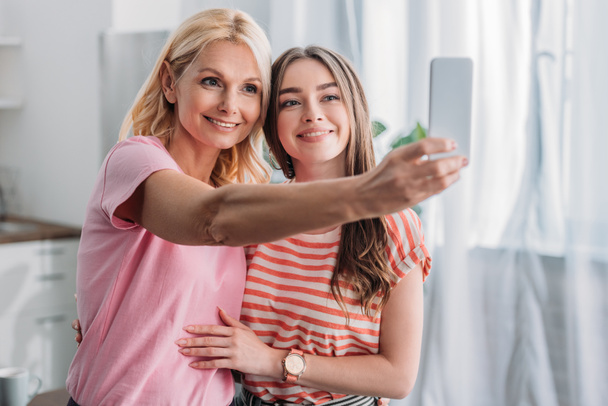 mooi, jong meisje knuffelen gelukkig moeder het nemen van selfie op smartphone  - Foto, afbeelding