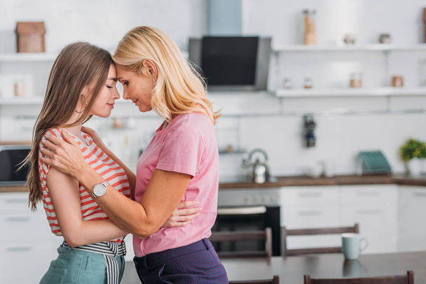 happy mother and daughter embracing while standing face to face in kitchen - Fotografie, Obrázek