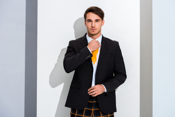handsome man touching yellow tie on white and grey  - Fotoğraf, Görsel