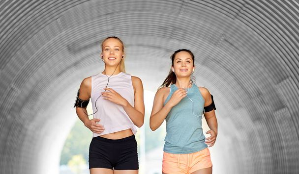 young women with earphones and smartphones running - Valokuva, kuva