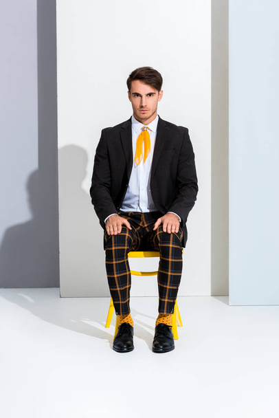 handsome and stylish man sitting on yellow chair on white and grey  - Foto, afbeelding
