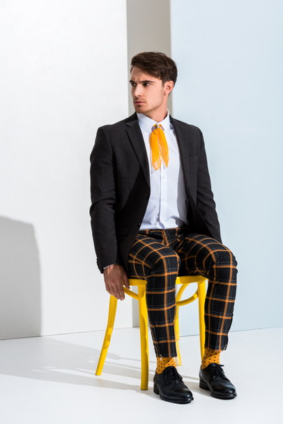 stylish man sitting on yellow chair on white and grey  - 写真・画像