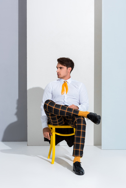 handsome man posing while sitting on yellow chair on white and grey  - Fotó, kép