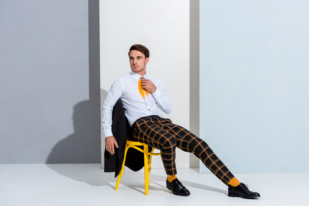 man in checkered trousers sitting on yellow chair on white and grey  - Photo, Image