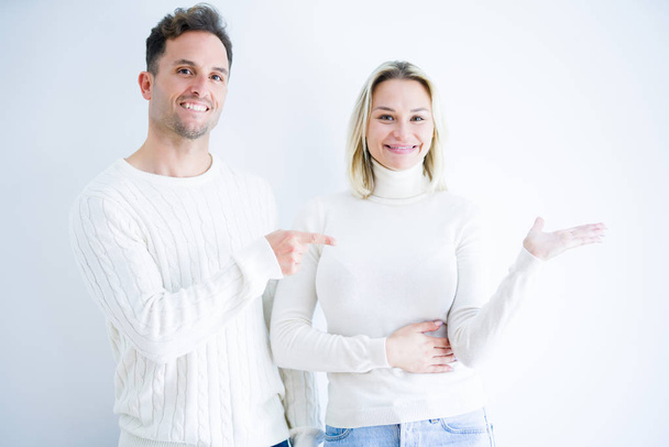 Young beautiful couple wearing casual t-shirt standing over isolated white background amazed and smiling to the camera while presenting with hand and pointing with finger. - Photo, Image