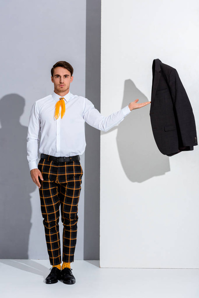 handsome man in checkered trousers standing and gesturing on white and grey  - Photo, Image