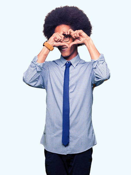 Jonge Afro-Amerikaanse business man met afro haar bril doen hart vorm met de hand en vingers glimlachend op zoek via Aanmeldingstoepassing - Foto, afbeelding