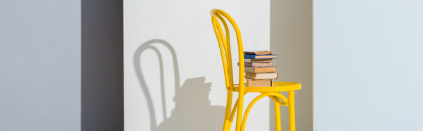 πανοραμική φωτογραφία της κίτρινης καρέκλας με βιβλία σε λευκό και γκρι  - Φωτογραφία, εικόνα