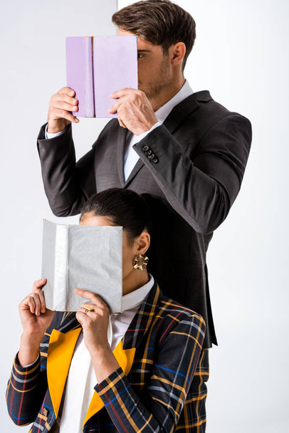 Stilvolle Männer und Frauen, die Gesichter bedecken, während sie Bücher auf weiß halten  - Foto, Bild