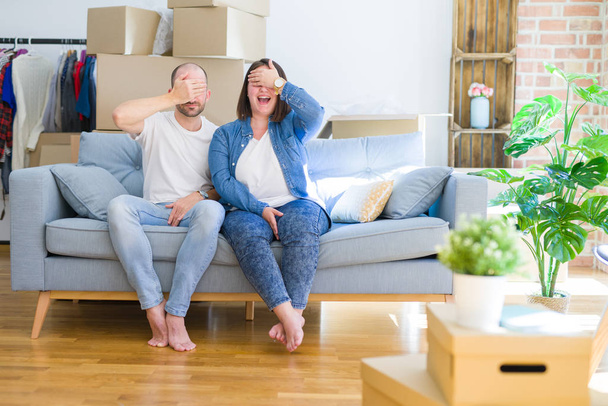 Ein junges Paar sitzt auf dem Sofa um Pappkartons herum und zieht lächelnd in ein neues Haus um. Blindes Konzept. - Foto, Bild