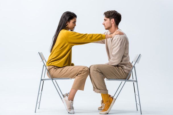 side view of attractive girl sitting on chair and touching man on white  - Photo, Image