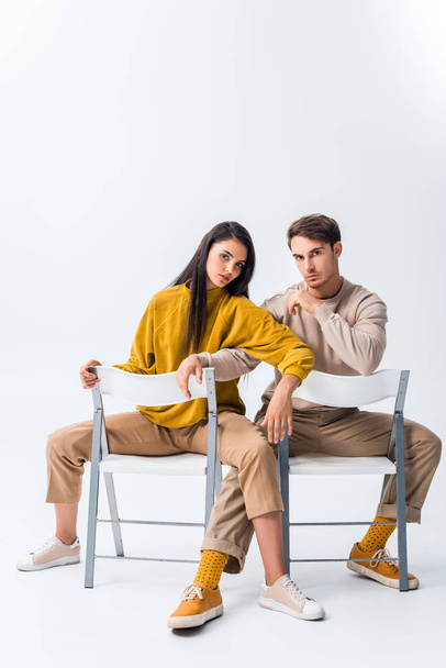 hombre guapo sentado en la silla y posando con chica atractiva en blanco
  - Foto, imagen
