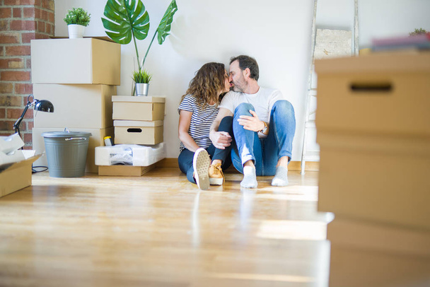 Orta yaş üst düzey romantik çift etrafında karton kutular ile daire katında oturan ve yeni bir eve taşınmak için mutlu gülümseyen aşk - Fotoğraf, Görsel