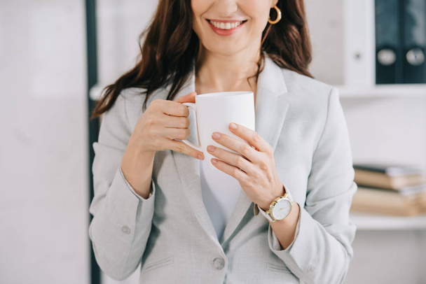 cropped view of smiling secretary holding coffee cup in office - Foto, Bild