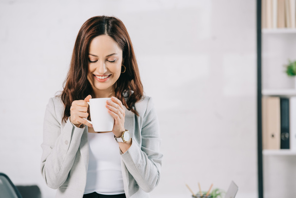 attractive, young secretary smiling while holding coffee cup in office - Foto, Bild