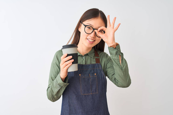 chinês barista mulher vestindo avental óculos beber café sobre isolado branco fundo com feliz rosto sorrindo fazendo ok sinal com mão no olho olhando através de dedos
 - Foto, Imagem
