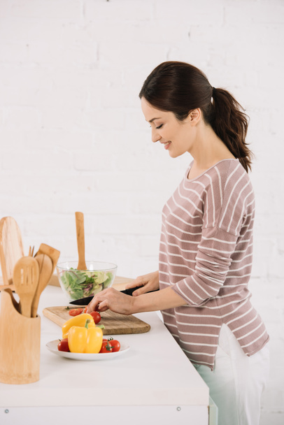 молода усміхнена жінка нарізає свіжі овочі на дошці
 - Фото, зображення