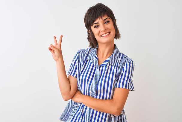 Young beautiful woman wearing blue striped shirt standing over isolated white background smiling with happy face winking at the camera doing victory sign. Number two. - Photo, Image