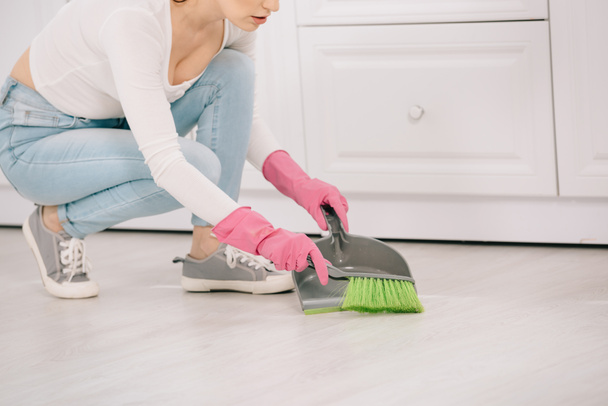 vista cortada de jovem dona de casa varrendo chão com escova e colher
 - Foto, Imagem