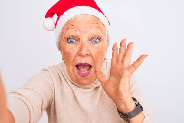 Сіроволоса жінка в Crhistmas Santa hat робить селфі над ізольованим білим фоном дуже щасливим і збудженим, переможний вираз, що вшановує перемогу з великою посмішкою і піднятими руками. - Фото, зображення