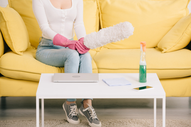 cropped view of housewife sitting on yellow sofa and holding dusting brush - Foto, immagini