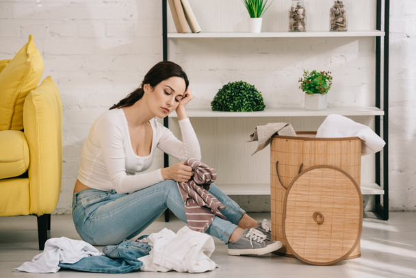 tired housewife sitting on floor near clothes and laundry basket - Valokuva, kuva