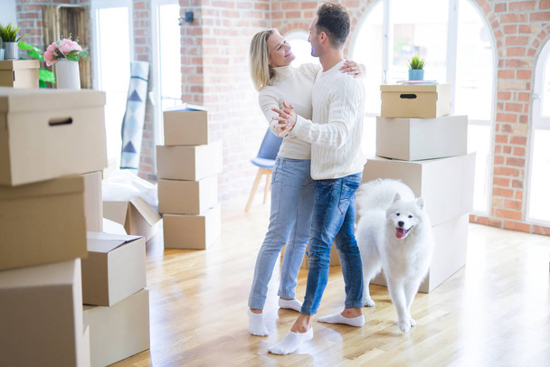 Young beautiful couple with dog dancing at new home around cardboard boxes - Photo, Image