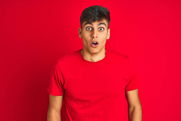 Giovane indiano indossa t-shirt in piedi sopra isolato sfondo rosso spaventato e scioccato con espressione a sorpresa, paura e viso eccitato
. - Foto, immagini