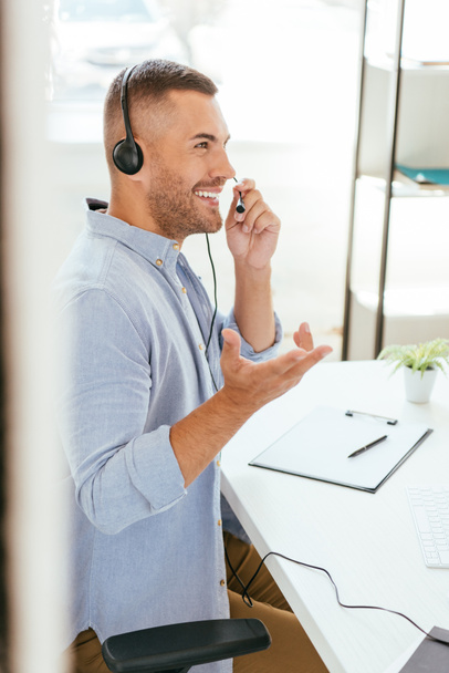 selective focus of happy broker touching headset and gesturing on office  - Photo, Image