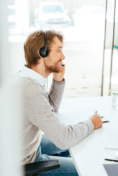 selective focus of happy bearded operator in brokers agency touching headset  - 写真・画像