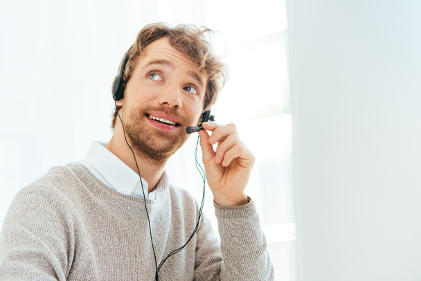 handsome bearded operator in brokers agency smiling and touching headset - Fotoğraf, Görsel
