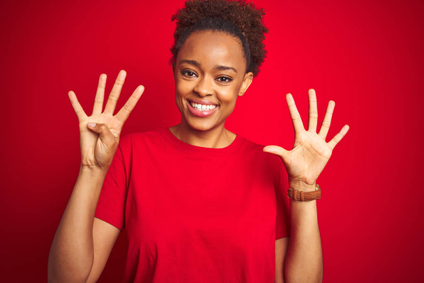 Giovane bella donna afro-americana con i capelli afro su sfondo rosso isolato mostrando e indicando con le dita il numero nove, sorridendo fiducioso e felice
. - Foto, immagini