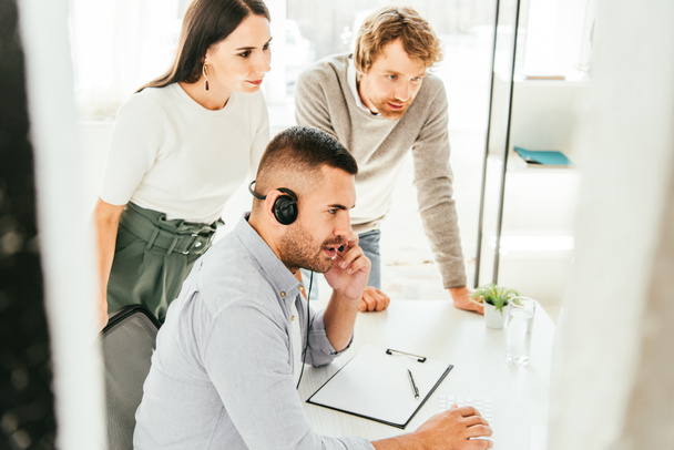 selectieve focus van makelaar in headset praten in de buurt van collega 's in kantoor  - Foto, afbeelding