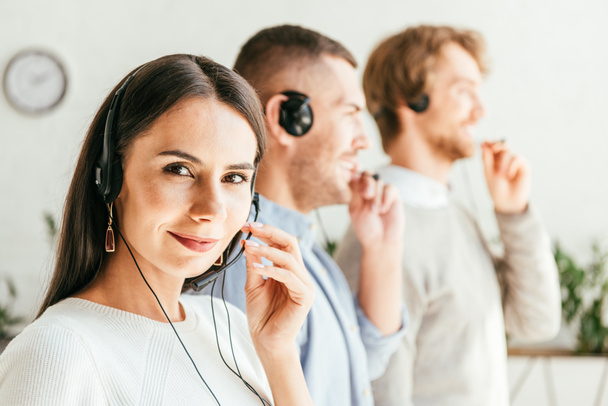 selective focus of attractive broker touching headset near men in office  - Photo, Image