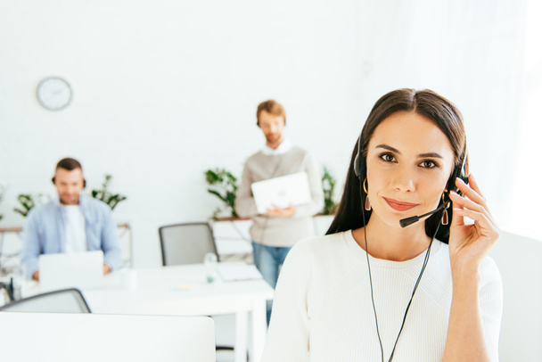 selective focus of beautiful broker touching headset while working with coworkers  - Foto, Bild