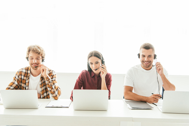 happy brokers in headsets working near laptops  - Foto, Imagen