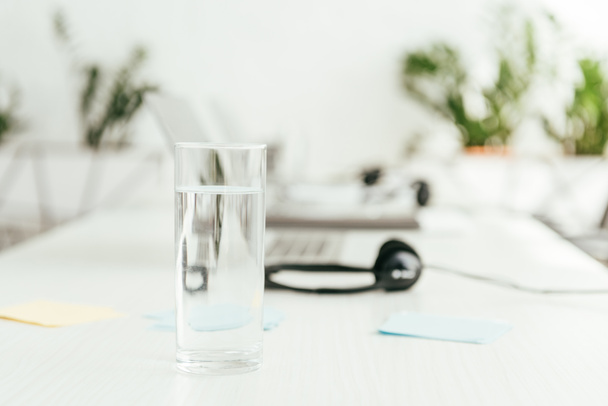 селективный фокус стекла с водой возле наушников в офисе
  - Фото, изображение