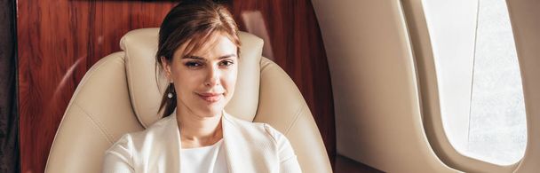 Panoramaaufnahme einer attraktiven Geschäftsfrau, die im Privatflugzeug lächelt  - Foto, Bild