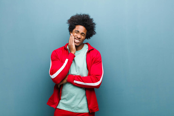 young black sports man holding cheek and suffering painful toothache, feeling ill, miserable and unhappy, looking for a dentist against grunge wall - Фото, изображение
