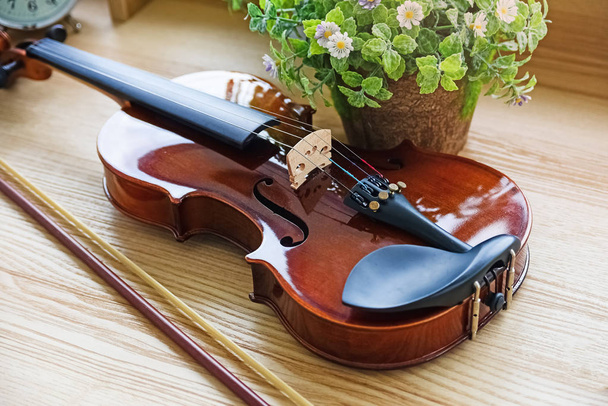 Le violon classique posé sur un bureau en bois, à côté du pot à fleurs, montre la face avant de l'instrument à cordes, la lumière floue autour - Photo, image