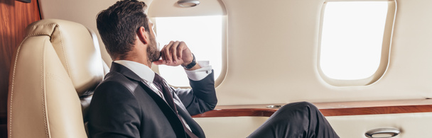 plano panorámico de hombre de negocios en traje mirando a través de la ventana en avión privado
  - Foto, Imagen