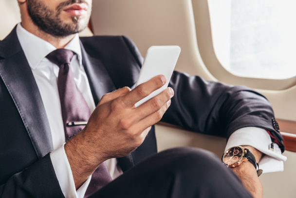 przycięty widok biznesmena w garniturze za pomocą smartfona w prywatnym samolocie  - Zdjęcie, obraz