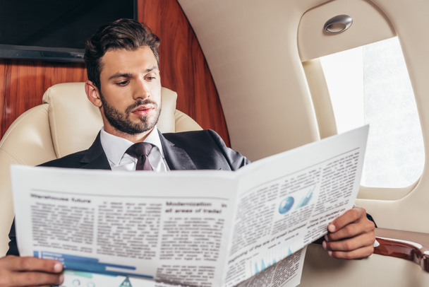 handsome businessman in suit reading newspaper in private plane  - Фото, изображение