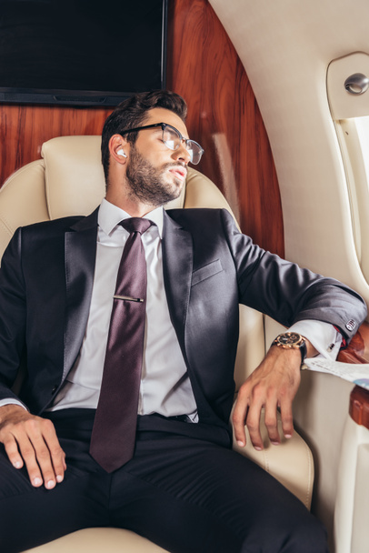 handsome businessman in suit sleeping and listening music in private plane  - Valokuva, kuva