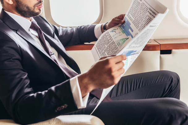cropped view of businessman in suit reading newspaper in private plane  - 写真・画像