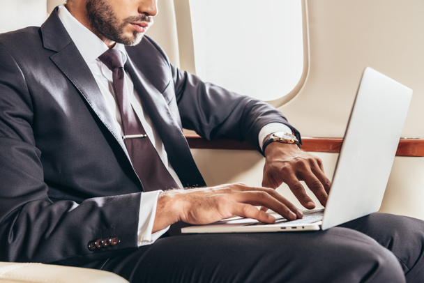 vista recortada de hombre de negocios en traje usando portátil en avión privado
  - Foto, Imagen