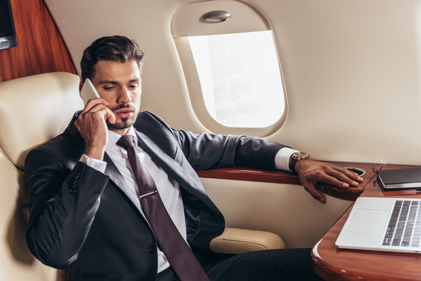 handsome businessman in suit talking on smartphone in private plane  - Foto, afbeelding